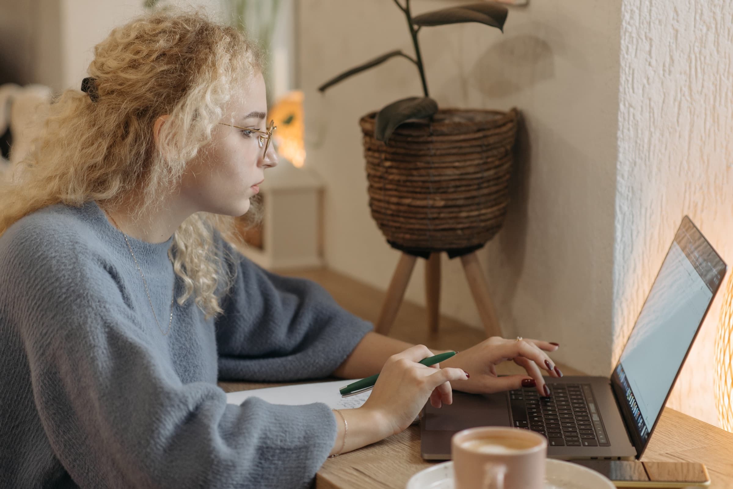 A student working through practice at a laptop, pen and notebook beside her
